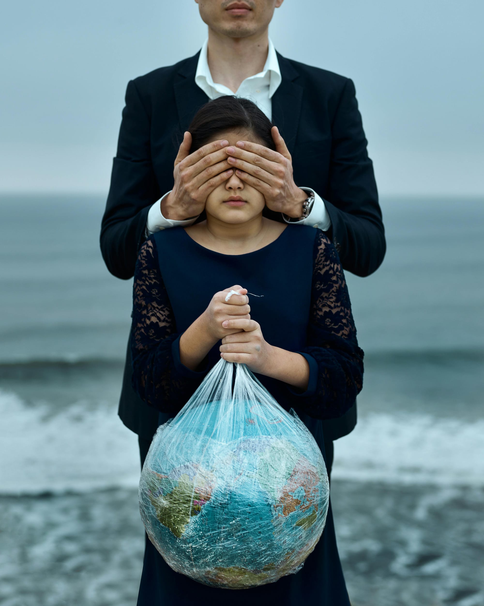 Representational Image of a child holding a globe wrapped in a plastic as a man behind her obstructs her vision with his hands.