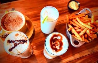 AMA Cafe food spread with milkshakes, iced coffee, hot chocolate, and crispy French fries with mustard dip on a wooden table.
