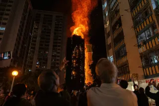 Onlookers observe as flames consume a building at Wang Fuk Court, Hong Kong, following a massive fire.