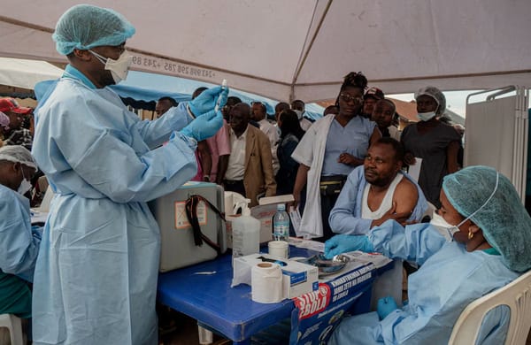 Health workers in the DRC wearing blue protective gear gather outdoors to receive Ebola vaccinations.